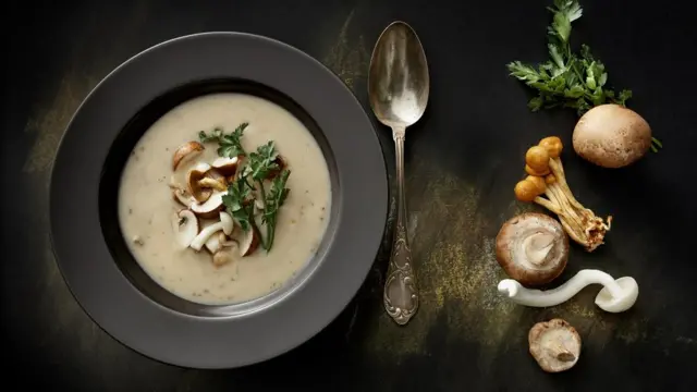 plate of mushroom soup, with spoon and wild mushrooms next to it