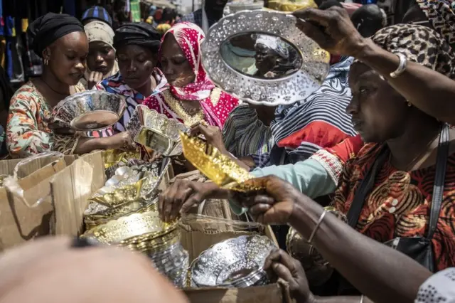Women buy bowls and plates at a market.