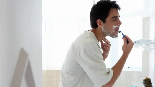 Seorang pria bercukur di depan cermin.