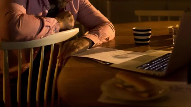 شاب يطالع ورقة وأمامه جهاز كمبيوتر محمول