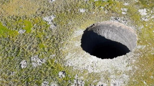 Cratera na tundra, vista de longe: um enorme buraco escurto e profundo