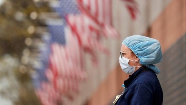 A nurse wearing personal protective equipment watches an ambulance driving away outside of Elmhurst Hospital during the ongoing outbreak of the coronavirus disease (COVID-19) in the Queens borough of New York, U.S., April 20, 2020