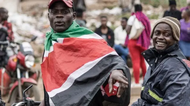 A boda-boda (motorcycle taxi) driver wears a Kenyan national flag as he drives a customer through the alleys of Kibera in Nairobi, on August 11, 2022