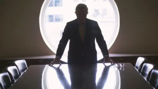 An authoritative man standing in a ditotrial manner on a meeting table