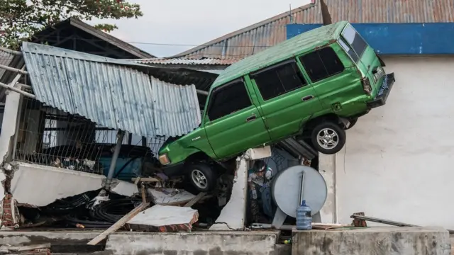 A man squeezes out from beneath a car that has been wedged into a building by a tsunami, on October 01, 2018 in Palu, Indonesia.