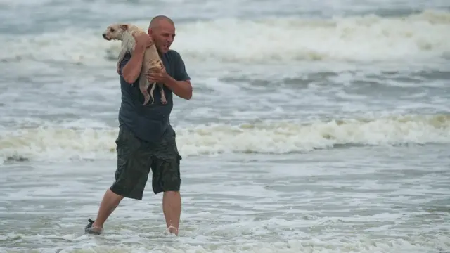 Homem sai do mar com um cachorro no colo