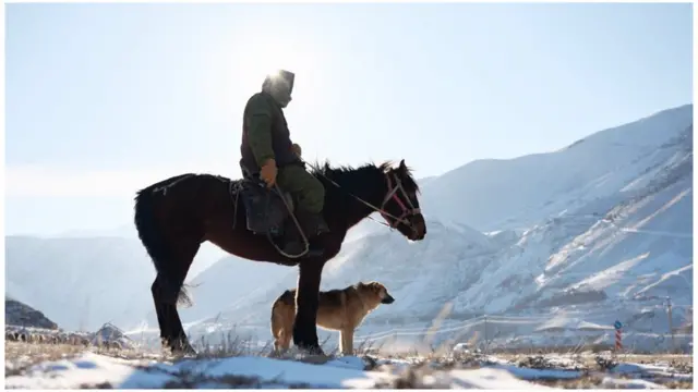 Homme à cheval et chien à ses côtés dans les montagnes enneigées du Kirghizistan
