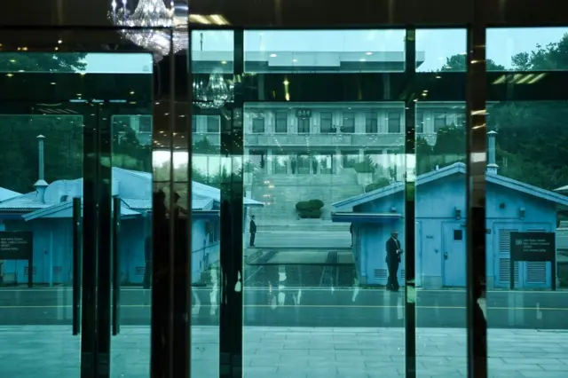 ترامپ پشت این در شیشه‌ای منتظر ماند تا به سوی مرز حرکت کند. کیم جونگ اون نیز باید از ساختمان روبه‌رو به سوی مرز می‌آمد. مرز بین دو ساختمان آبی قرار دارد