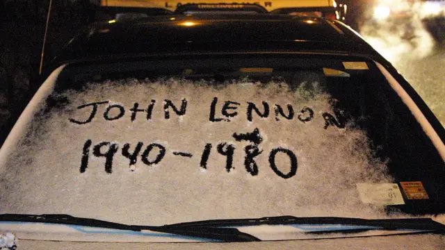 El nombre de John Lennon con su fecha de nacimiento y muerte escrito en la nieve sobre el parabrisas de un auto.