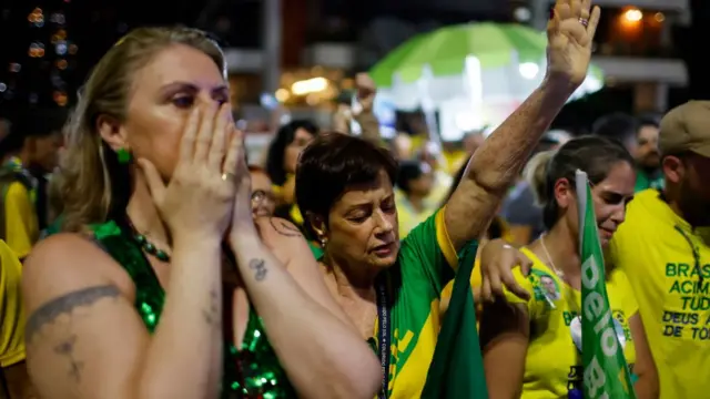 Mulheres vestidas com cores da bandeira do Brasil choram e oram