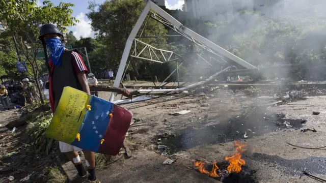 Un manifestante con un escudo improvisado que lleva la bandera de Venezuela pintada.