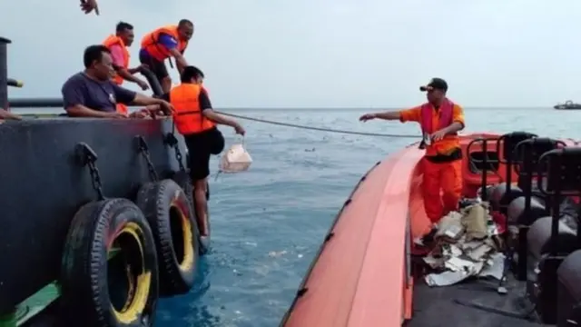 رجال الإنقاذ يجمعون متعلقات، من بينها حقيبة يد، وحطام من منطقة تحطم الطائرة المشتبه به