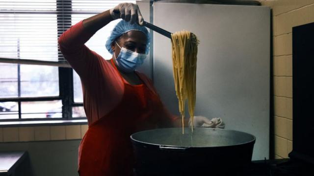 Mulher usa máscara e touca no cabelo enquanto cozinha macarrão no bairro do Bronx, Nova York