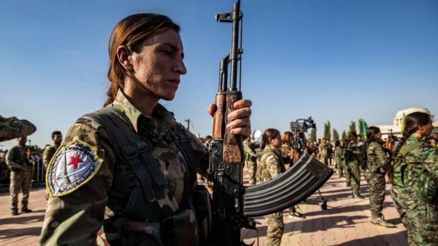 Kurdish fighter stands with gun at funeral in Derik on 13 October 2019