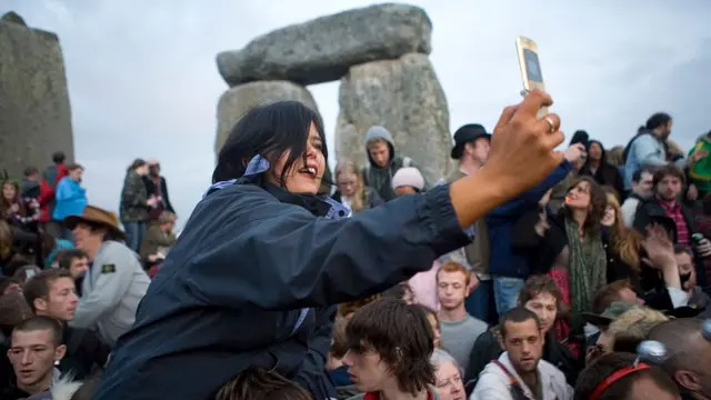 Uma mulher usa o celular para tirar uma foto, na árearoda roletaStonehenge, cheiaroda roletapessoas