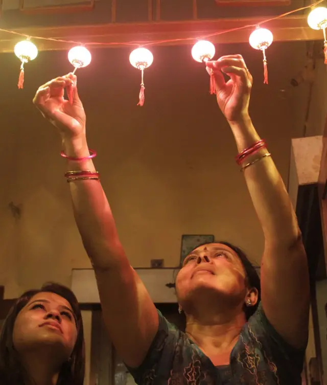 ઘરનાં દ્વારે એલઇડી લાઇટનું તોરણ લગાવતી મહિલા