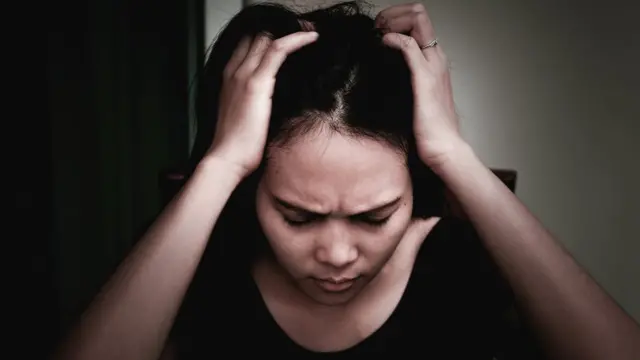 Una mujer se sujeta la cabeza y tiene cara de preocupación