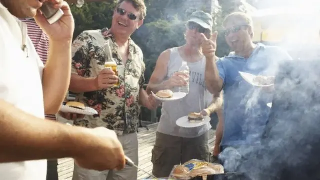Hombres en una barbacoa comiendo hamburguesas y bebiendo cerveza y agua.