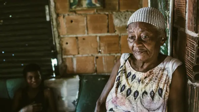 Mulher negraesporte da sorte bancalenço na cabeça com olhar triste, com menino sorridente ao fundo