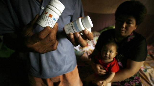 AIDS sufferers Cao Xiaonian (L) shows his medicine whilst his wife Zhou Xiaoneng (R) holds their 9-month-old baby in their village home in China's southern Henan province 02 August 2006