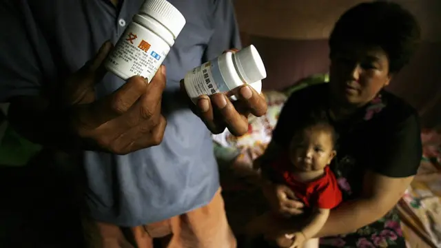 AIDS sufferers Cao Xiaonian (L) shows his medicine whilst his wife Zhou Xiaoneng (R) holds their 9-month-old baby in their village home in China's southern Henan province 02 August 2006