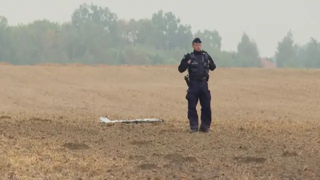 Polski policjant stoi obok fragmentu bezzałogowego statku powietrznego (UAV), po tym jak rosyjskie drony naruszyły polską przestrzeń powietrzną podczas ataku na Ukrainę