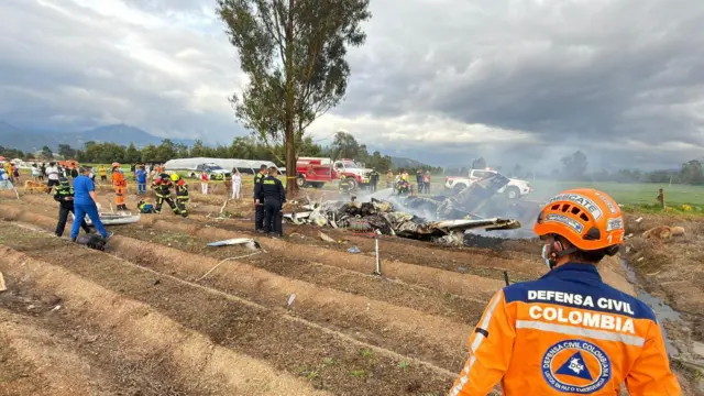 Los restos de una avióneta humana accidentada mientras decenas de personas uniformadas rodean el lugar.
