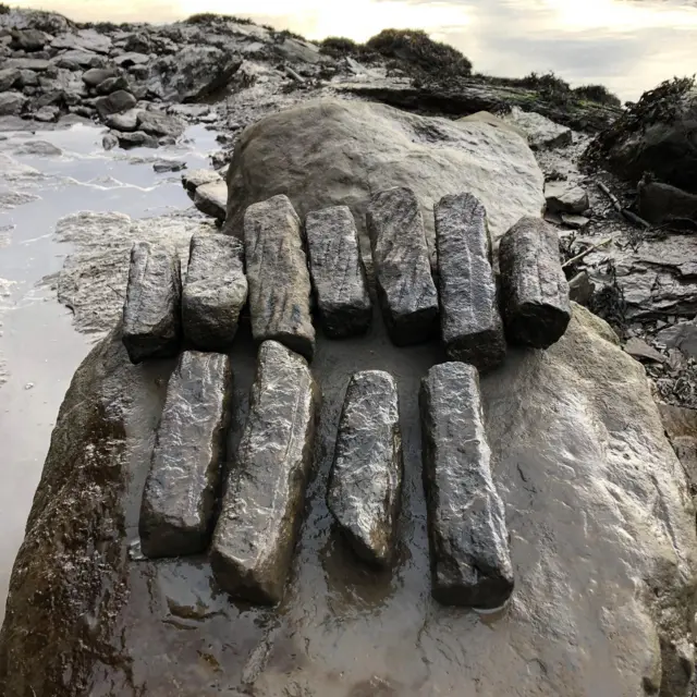 Algunas de las piedras de afilar halladas en la excavación. Son largas, oscuras y rectangulares. Tienen diferentes longitudes y se encuentran sobre una gran roca junto al río Wear.