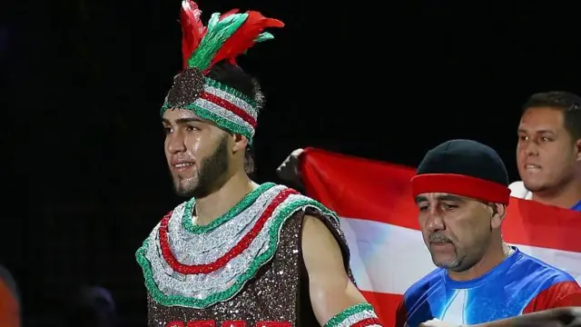 Prichard Colon wear sparkly red, silver and green vest and headband wit feathers