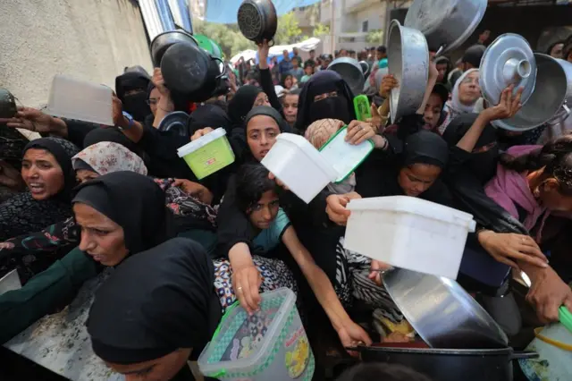 Mujeres y niñas con ollas y recipientes vacíos