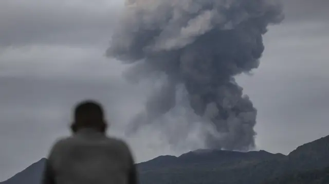 Um socorrista observa o vulcão Monte Dukono durante sua erupção em Halmahera Norte, Indonésia, em 9 de maio de 2026. De acordo com a agência de resgate da Indonésia (Basarnas), os socorristas recuperaram o corpo de um excursionista indonésio, enquanto dois excursionistas de Singapura continuam desaparecidos.
