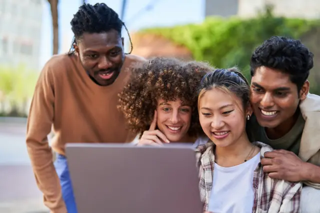 Cuatro jóvenes, hombres y mujeres, ven un programa en una computadora portátil 