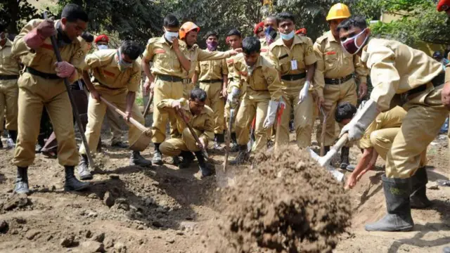 પાંદડાં નીચે ઢાંકી દેવાયેલી કબરોને શોધી રહેલાં ઢાકાના ફાયરમૅનોની તસવીર