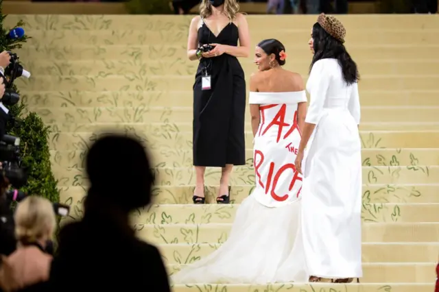 Ocasio-Cortez wearing a white dress with the words "Tax the Rich" emblazoned on the back