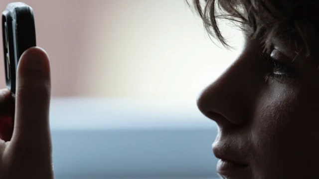 نیم رخ کودکی که موبایلی را از فاصله نزدیک به صورتش گرفته و به آن نگاه میکند