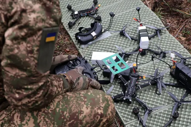 На карематі перед оператором з пультом керування розкладені FPV-квадрокоптери