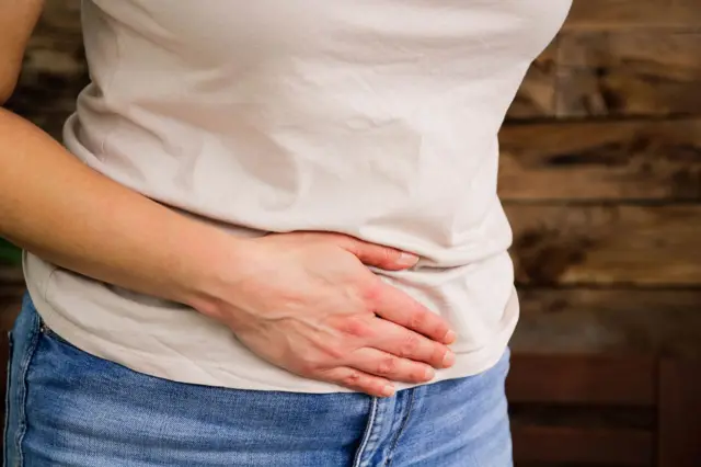 Stock image: a close-up of a woman with her hand across her stomach. She is wearing a light pink t-shirt and blue jeans.