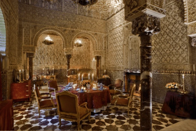 صورة داخلية لقاعة الطعام في القصر. طاولة دائرية مغطاة بمخمل أحمر فاخر ومجهزة للعشاء تتوسط المكان.