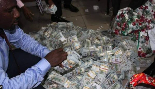 EFCC officer dey count moni as plenty bundles of dollar full for ground wey dem recova from one house for Ikoyi Lagos for April 2017.