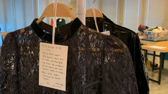 圖中是一件吊掛的黑色蕾絲上衣，上面附著一張手寫小卡。