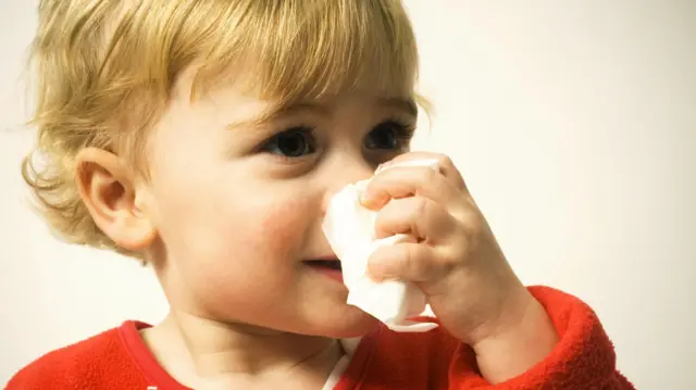 Mały chłopiec dmucha nos w chusteczkę.