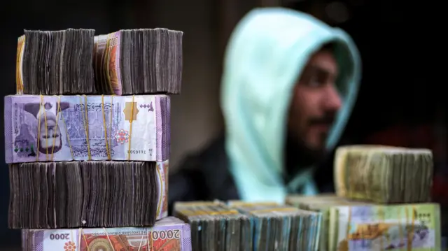 أكوام من الأوراق النقدية بالليرة السورية في كشك لصراف العملات في سوق بمدينة منبج في محافظة حلب شمال سوريا في 4 يناير/كانون الثاني 2025