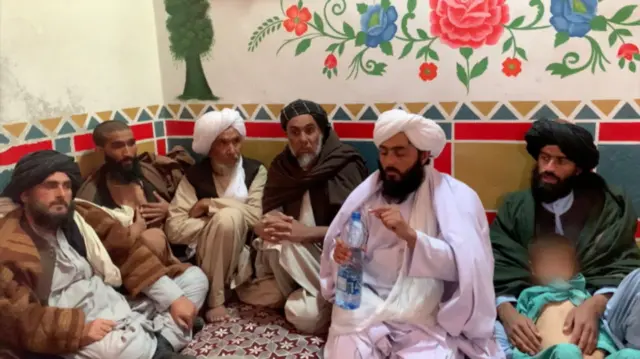 ندا قادری مرد حدود سی و پنج ساله در میان بیماران نشسته بوتل آب در دست دارد. مردانی هم متوجه به او در چهارطرفش نشسته اند. 
