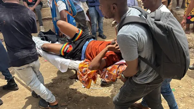 An injured man, in a brown shirt and black short, is carried on a stretcher