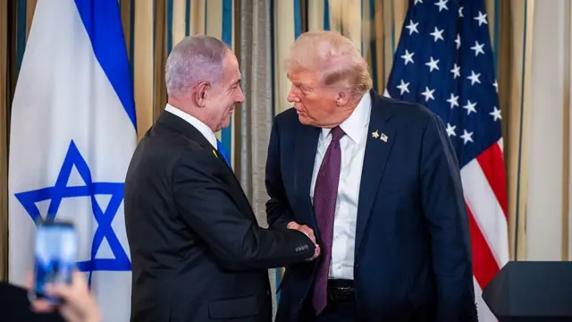 US President Donald Trump (right) and Israeli Prime Minister Benjamin Netanyahu, shake hands during a news conference on 29 September at the White House in Washington DC. Both are wearing suits and their countries' flags are displayed in the background.