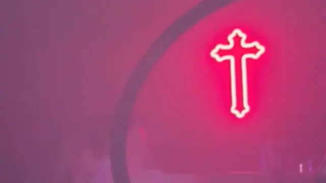 Una luz en forma de cruz de neón rosa colgada en una discoteca. 