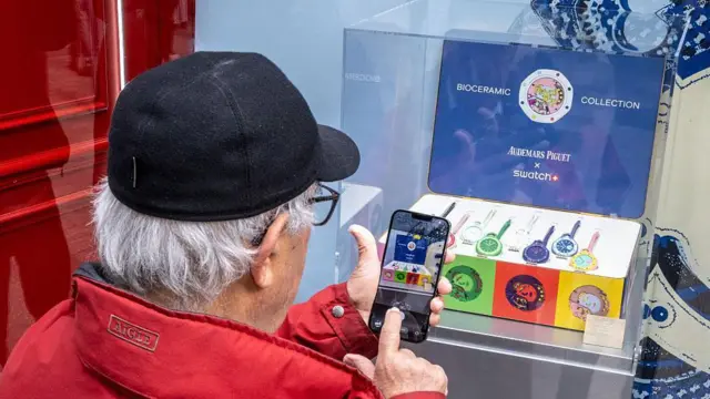 一名穿紅色外套、戴黑色帽子的人士,在巴黎用智能手機拍攝一個 Royal Pop Swatch 腕錶展示櫥窗