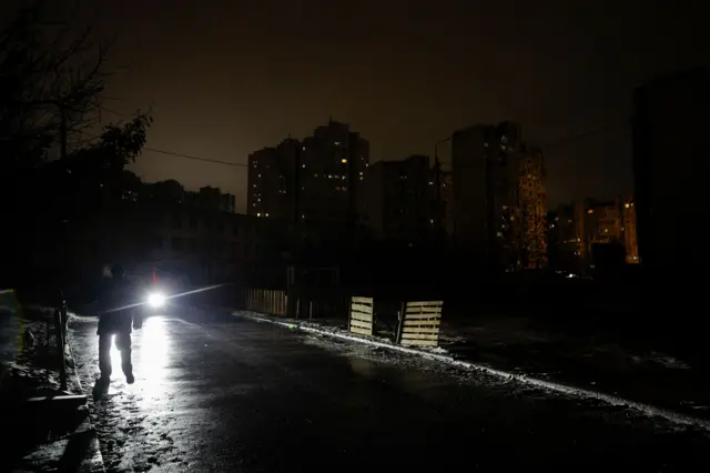 Темна вулиця, якої йде людина, її освітлюють лише фари авто