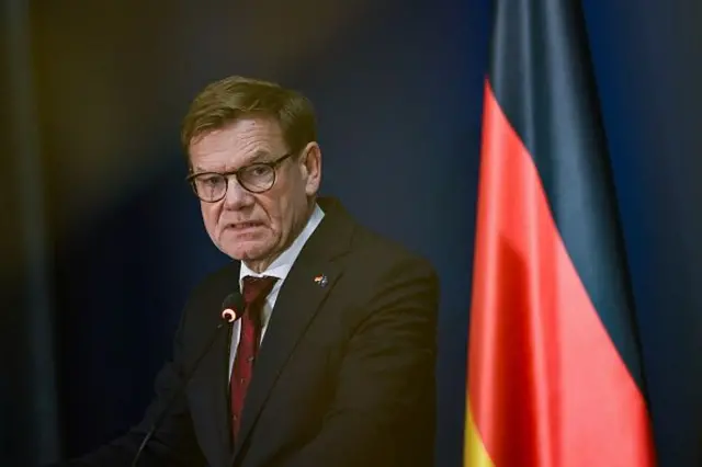 Wadephul siyah bir ceket, kırmızı bir kıravat giyinmiş, mikrofona konuşuyor arka planda Alman bayrağı görünüyor. 18 kasım 2025.