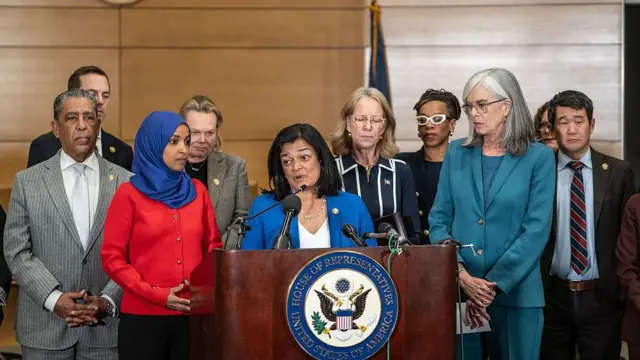 米連邦議会下院の標章がついた演台を前に、複数の議員が真剣な表情で立っている
